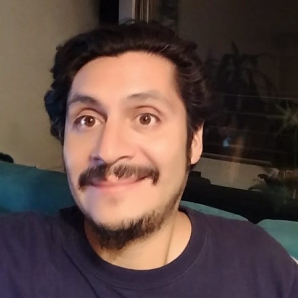 Blog Gus Fernández Hombre sonriente con cabello rizado, usando una camiseta oscura, posando en un entorno interior.